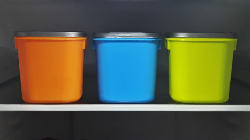 three plastic containers. From left to right, orange, blue and green