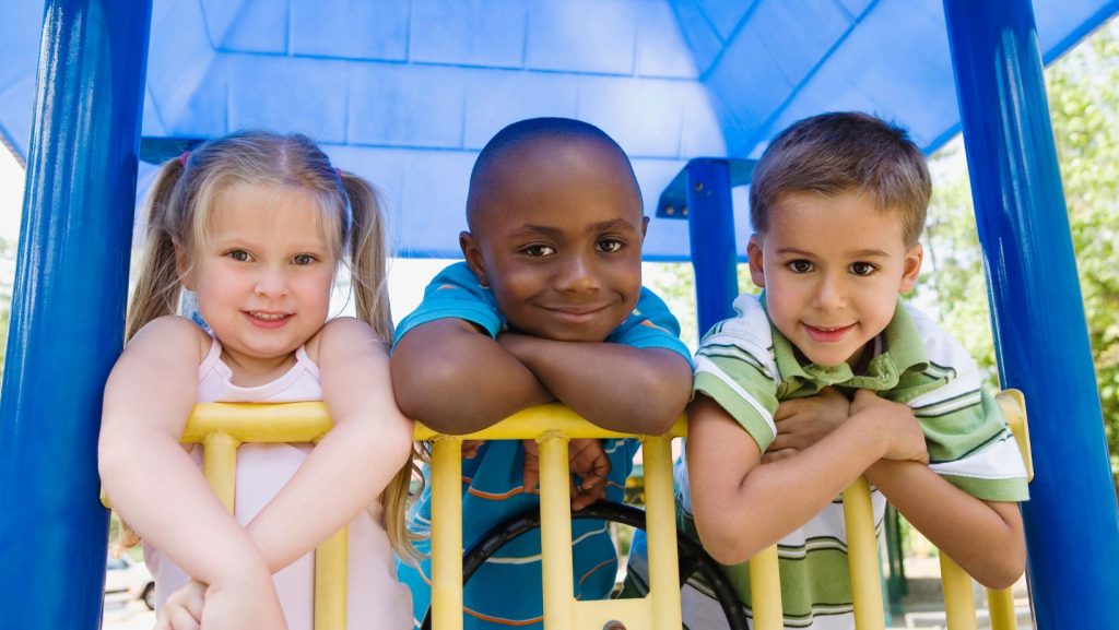 Three kids on a playground smiling